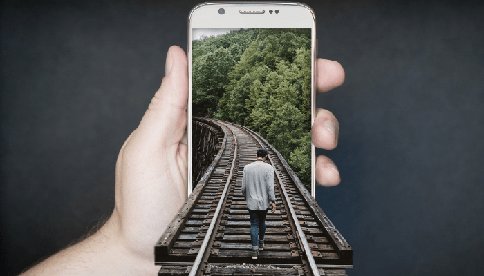 artistic photo of man walking into cell phone along train tracks